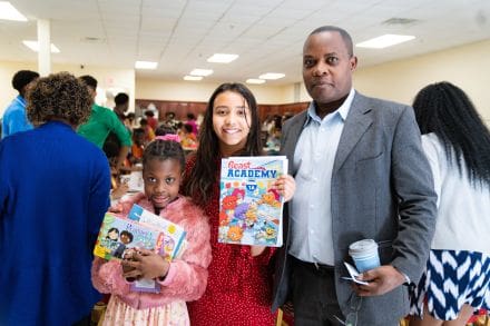 A man and two girls holding up books.